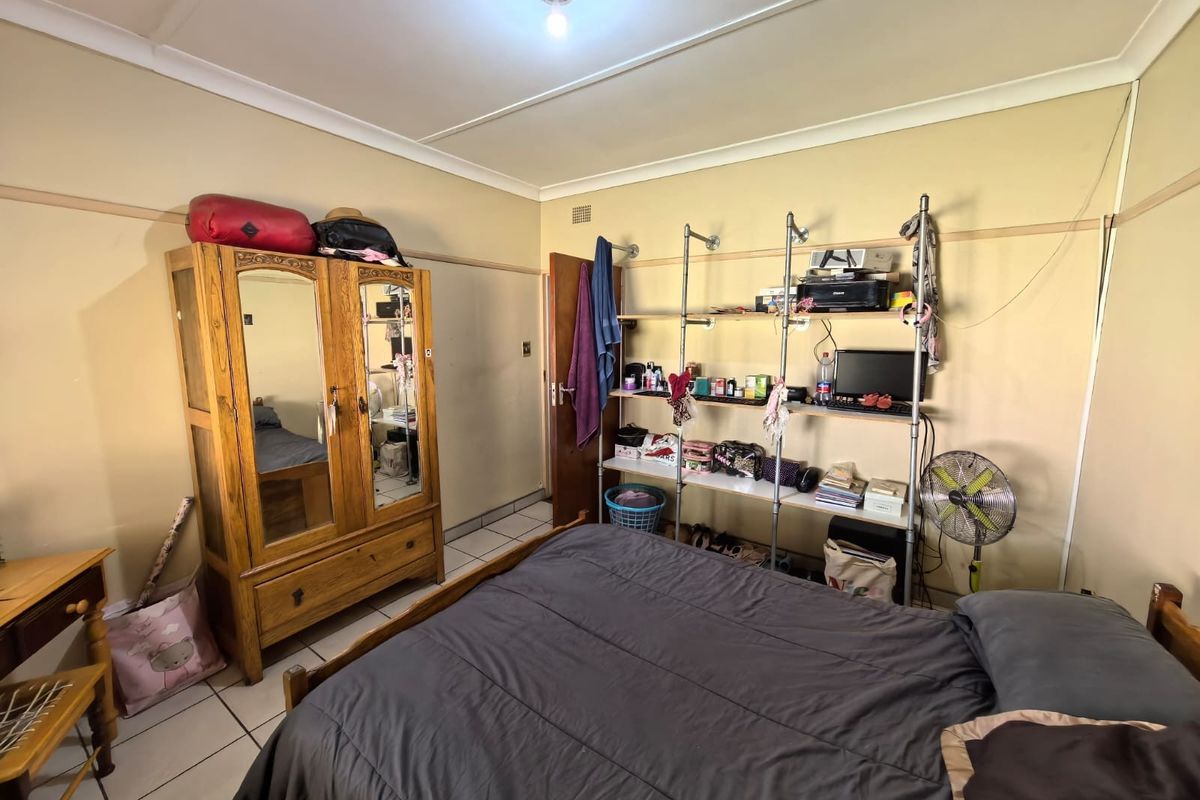 A bedroom featuring tiled flooring and coved ceilings, currently utilized as a sleeping and storage area.