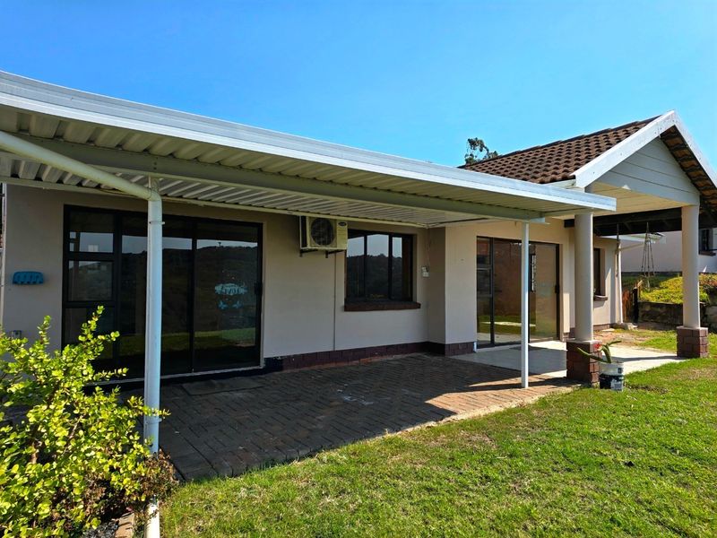 A covered outdoor patio area featuring paved flooring, sliding glass door access, and an external air conditioning unit, overlooking the garden.