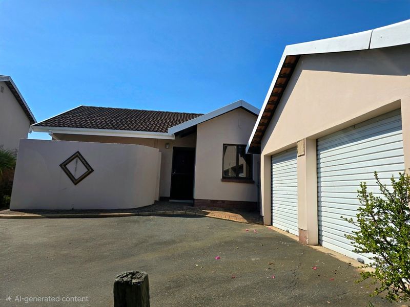 Front exterior view of a townhouse featuring a double garage, paved driveway, and a private entrance area with a boundary wall.