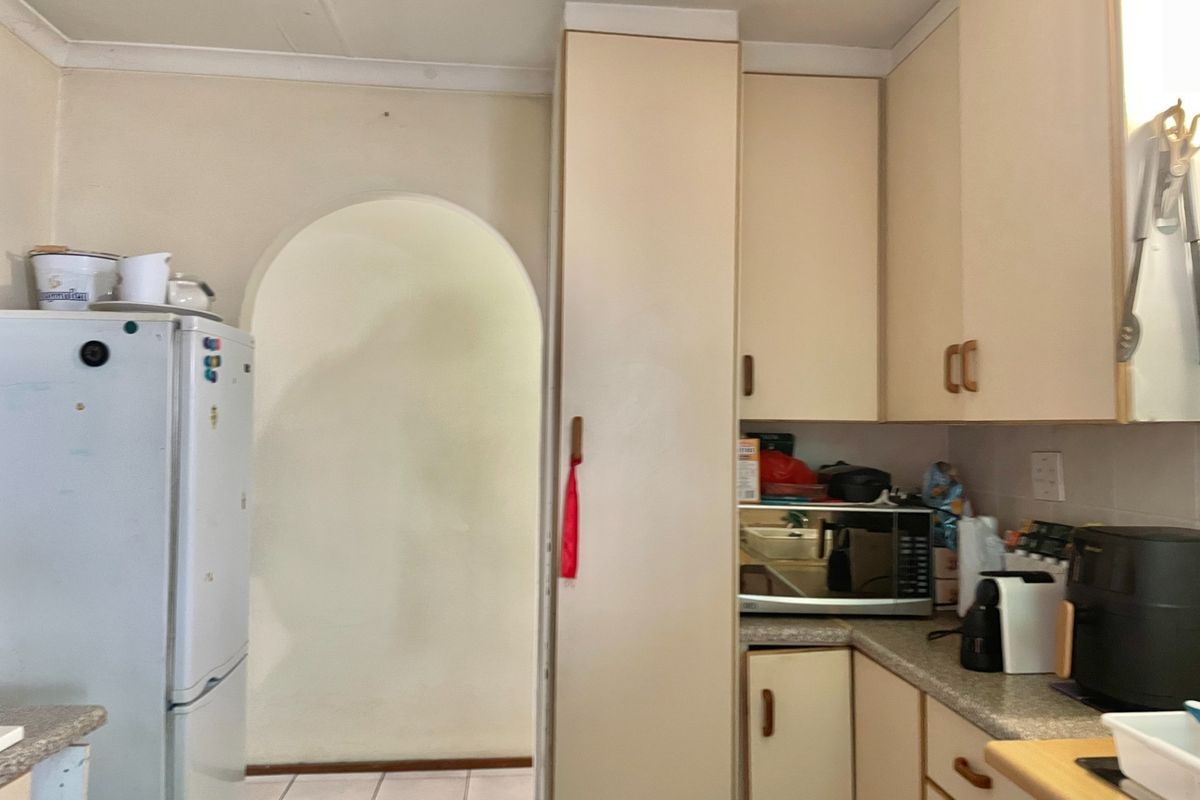 A dated kitchen featuring original built-in cabinetry, laminate countertops, and tiled flooring, leading through an arched doorway to the rest of the home.