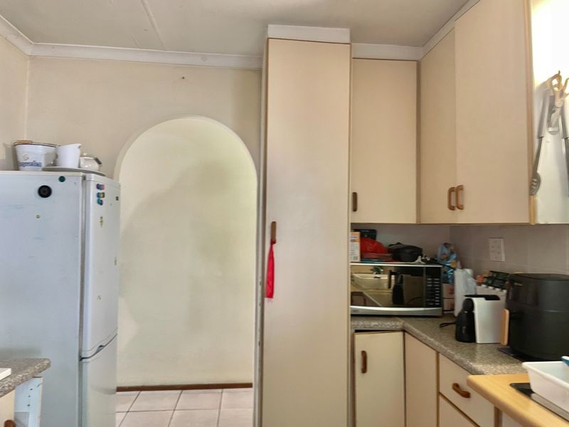 A dated kitchen featuring original built-in cabinetry, laminate countertops, and tiled flooring, leading through an arched doorway to the rest of the home.