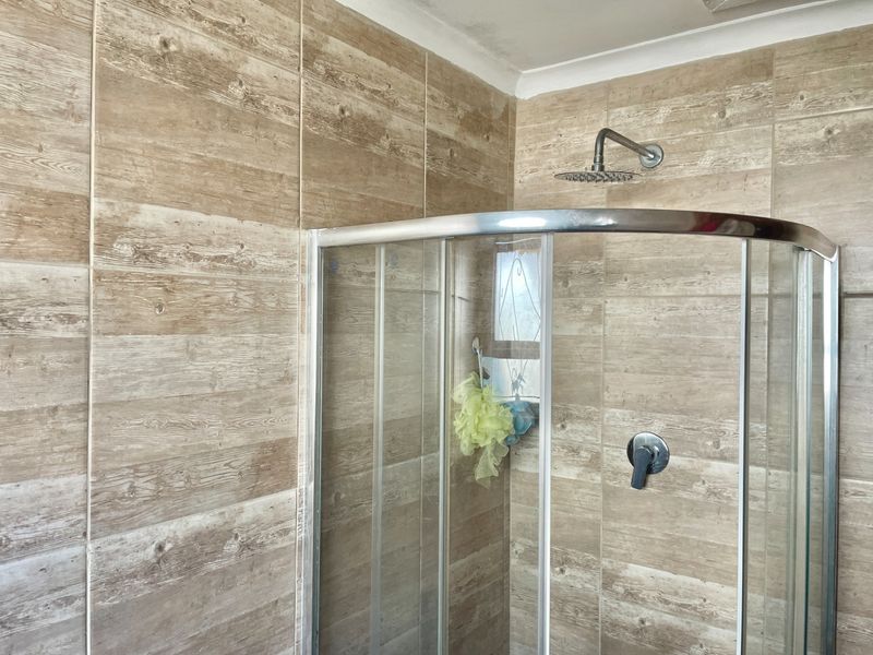 A modern bathroom shower area featuring wood-look ceramic wall tiles and a contemporary rain shower head with a glass enclosure.