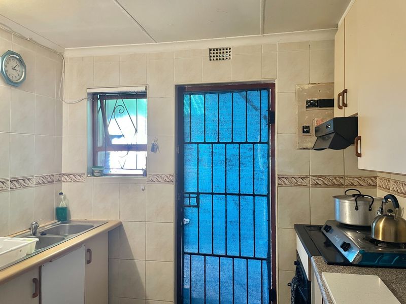A functional kitchen featuring tiled walls, built-in cabinetry, a double bowl sink, and a security gate leading to the exterior.