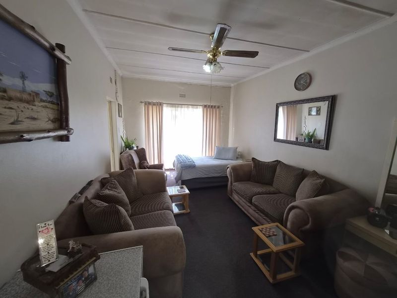 A living room area featuring a ceiling fan, carpeted flooring, and a sliding glass door leading to an adjacent space.