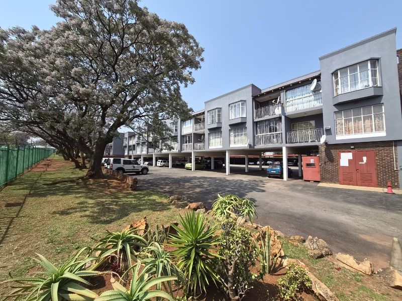 Exterior view of a multi-story apartment complex featuring covered ground-level parking, private balconies, and a paved driveway area.