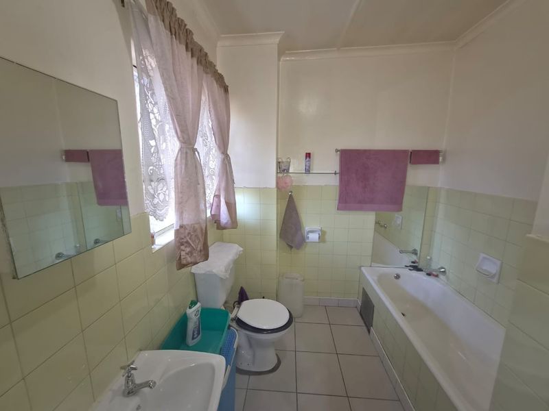 A functional bathroom featuring a bathtub, pedestal basin, and toilet with dated wall tiling and neutral floor tiles.