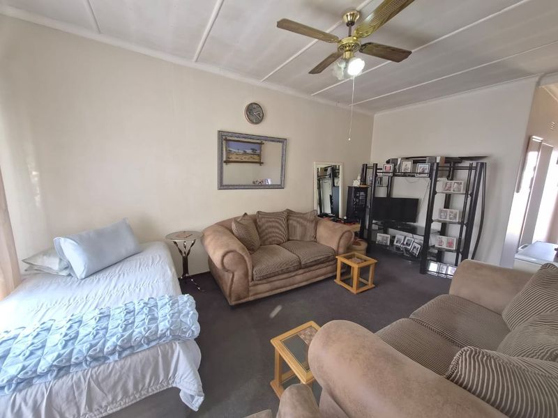 A living room area featuring a ceiling fan and carpeted flooring, offering a functional space with potential for modernization.