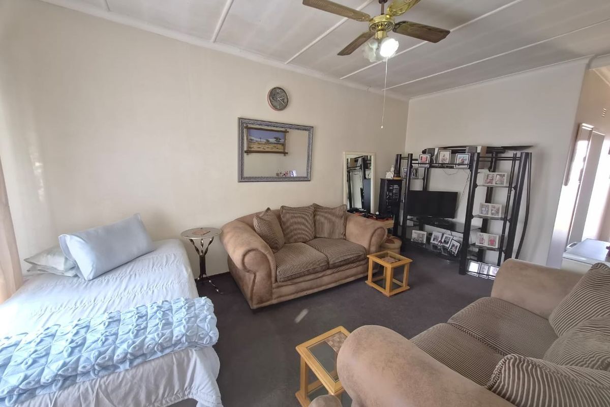 A living room area featuring a ceiling fan and carpeted flooring, offering a functional space with potential for modernization.