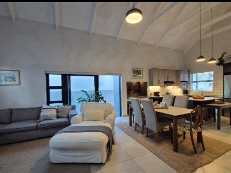 Spacious open-plan living and dining area featuring vaulted ceilings with exposed beams, tiled flooring, and a modern kitchen with a central island.