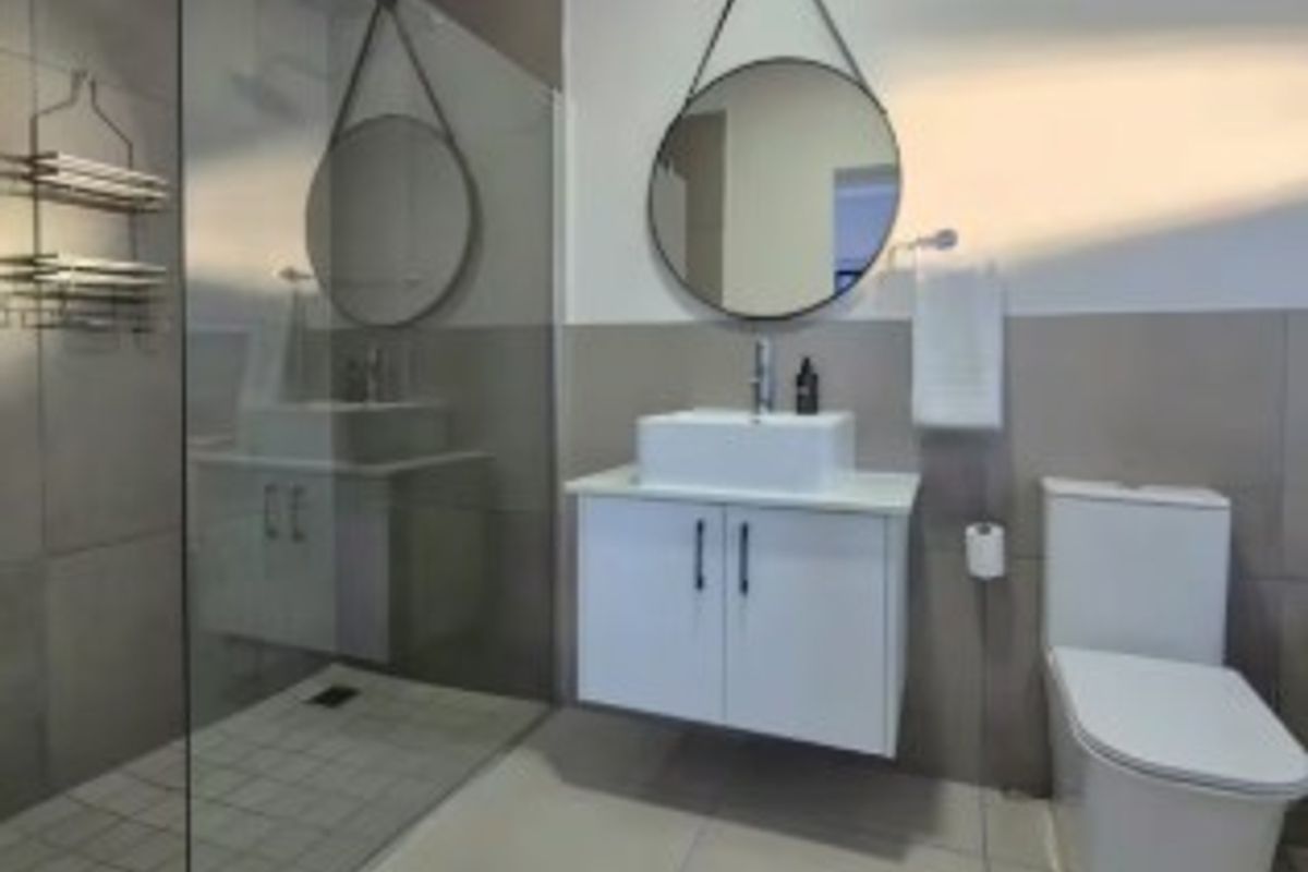 Modern bathroom featuring a walk-in shower with glass screen, wall-mounted vanity with vessel sink, and a contemporary toilet with neutral wall and floor tiling.