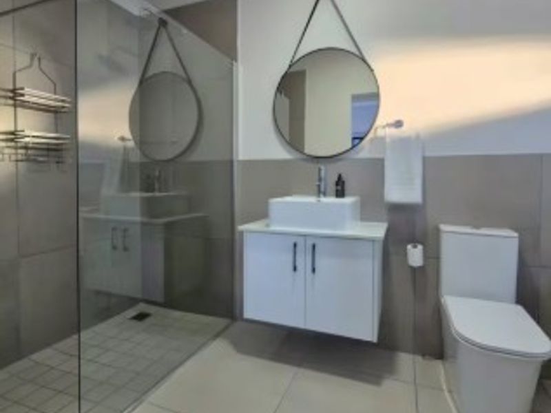 Modern bathroom featuring a walk-in shower with glass screen, wall-mounted vanity with vessel sink, and a contemporary toilet with neutral wall and floor tiling.