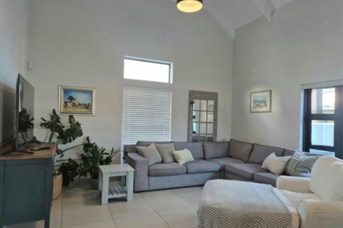 Spacious living room featuring high vaulted ceilings, large windows with venetian blinds, and neutral tiled flooring, creating a bright and airy atmosphere.