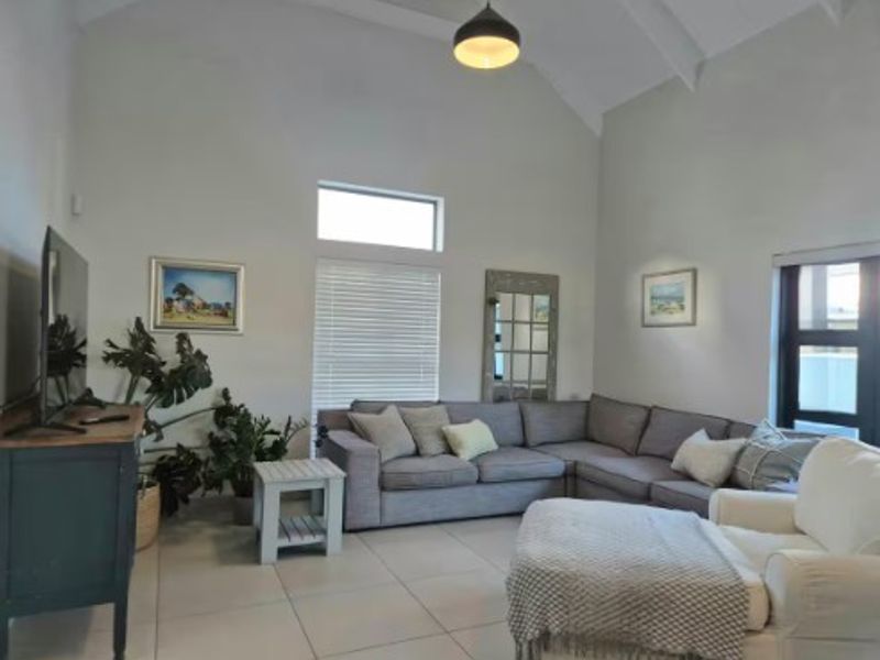 Spacious living room featuring high vaulted ceilings, large windows with venetian blinds, and neutral tiled flooring, creating a bright and airy atmosphere.