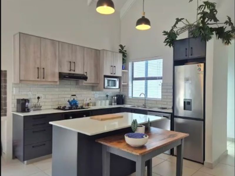 Modern kitchen featuring two-tone cabinetry, stone countertops, a central island, subway tile backsplash, and vaulted ceilings with pendant lighting.