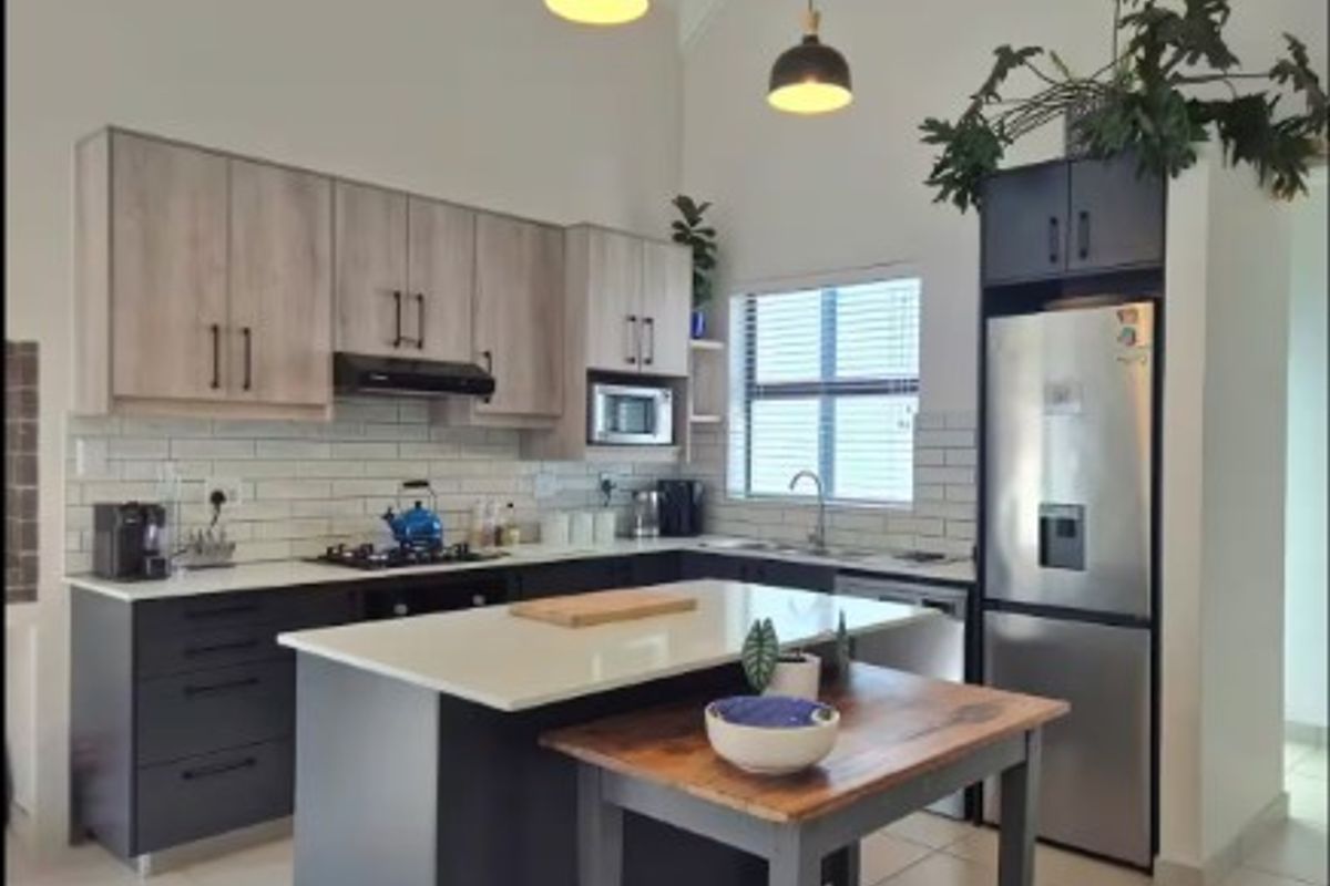 Modern kitchen featuring two-tone cabinetry, stone countertops, a central island, subway tile backsplash, and vaulted ceilings with pendant lighting.