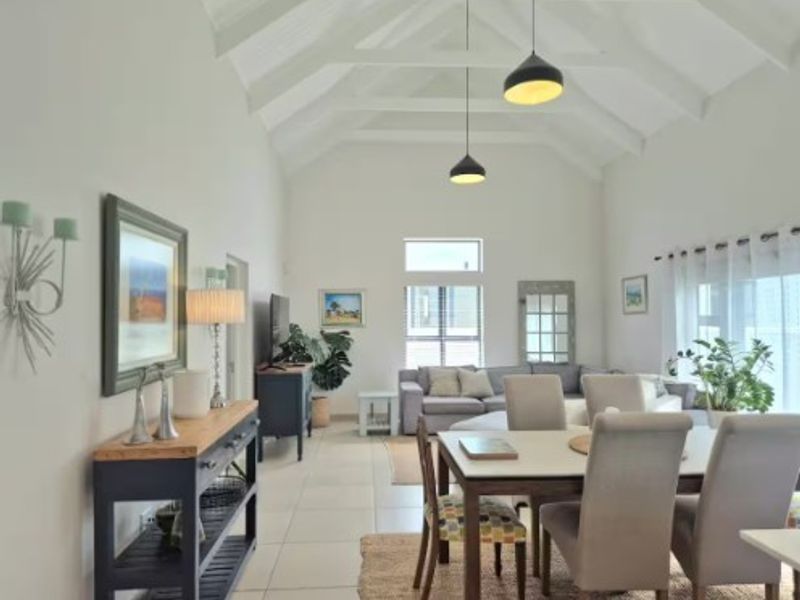 Spacious open-plan living and dining area featuring a high vaulted ceiling with exposed rafters, tiled flooring, and modern pendant lighting.