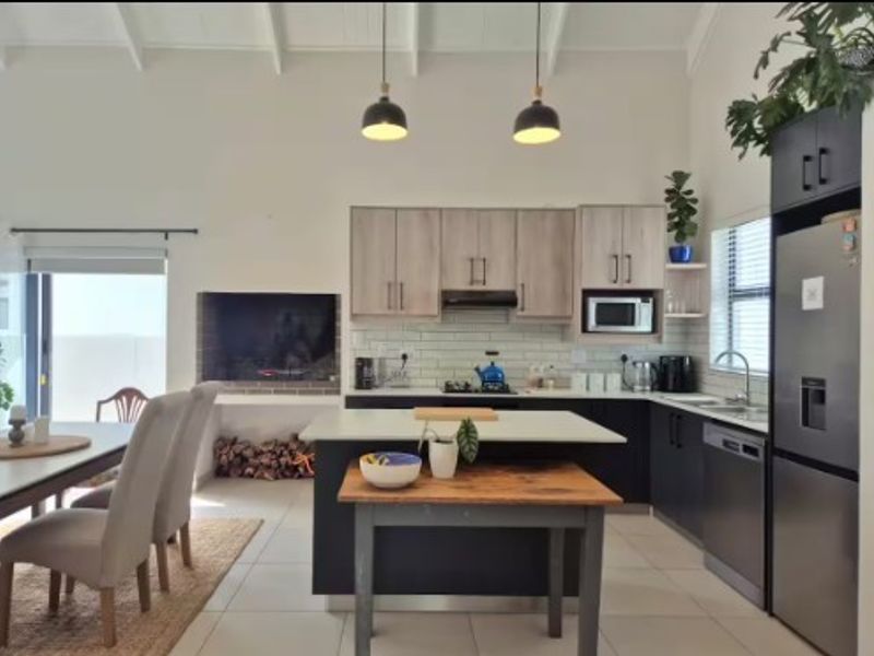 Modern open-plan kitchen and living area featuring a built-in fireplace, central island, contemporary cabinetry, and high vaulted ceilings.
