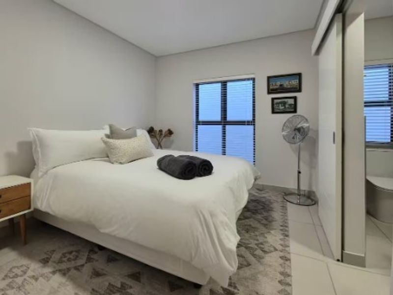 A well-maintained bedroom featuring neutral wall finishes, tiled flooring, and a convenient sliding door providing access to an en-suite bathroom.