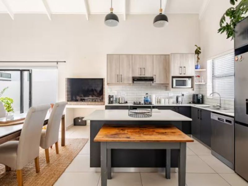 Modern open-plan kitchen and dining area featuring a central island, sleek cabinetry, subway tile backsplash, and a built-in fireplace under a vaulted ceiling.