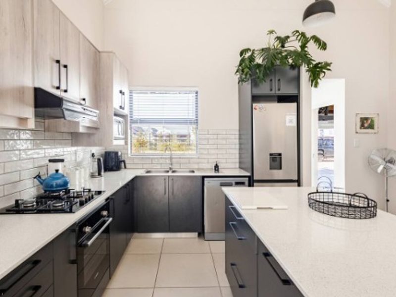 Modern kitchen featuring stone countertops, subway tile backsplash, gas hob, built-in oven, and ample cabinetry with a central island.