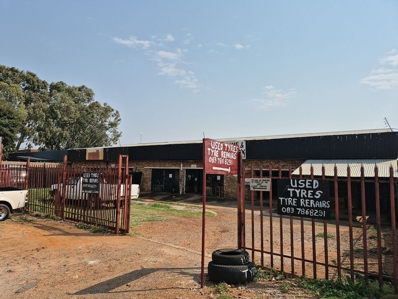 Front exterior view of an industrial property featuring a brick facade, corrugated metal roofing, and perimeter security fencing with multiple business signs.