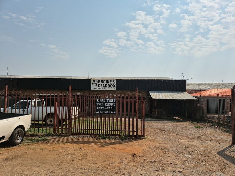 Front exterior view of an industrial workshop property featuring a brick facade, corrugated metal roofing, and secure perimeter fencing.