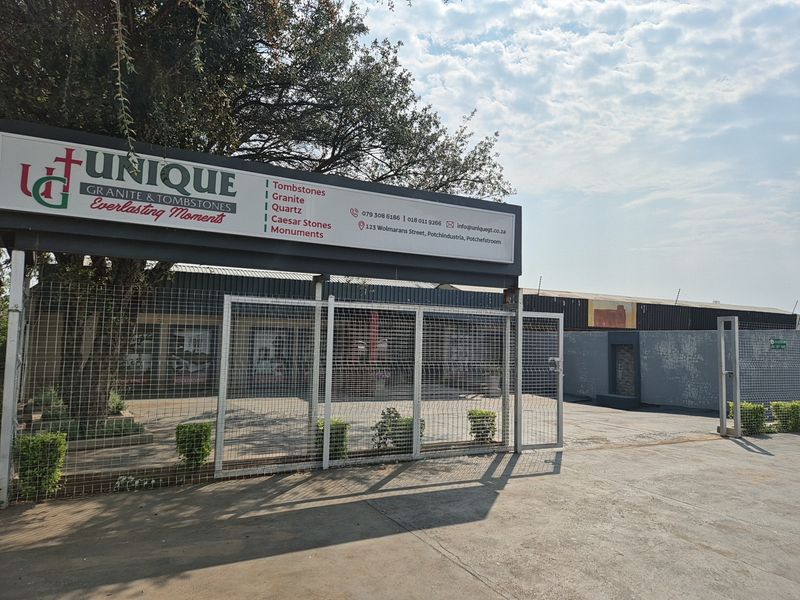 Front exterior view of an industrial property featuring a large business sign, concrete driveway, and secure metal fencing.