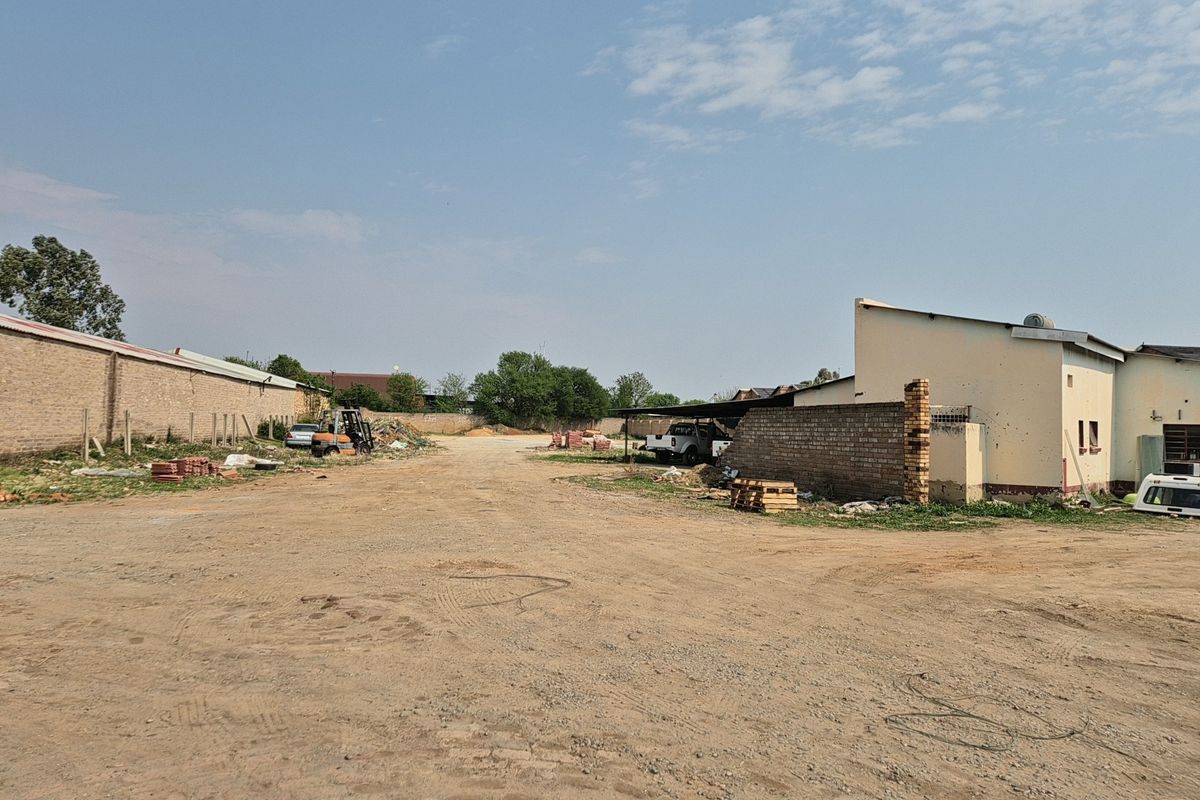 Expansive industrial yard area featuring a perimeter brick wall, covered parking structure, and large unpaved ground space suitable for storage or logistics.