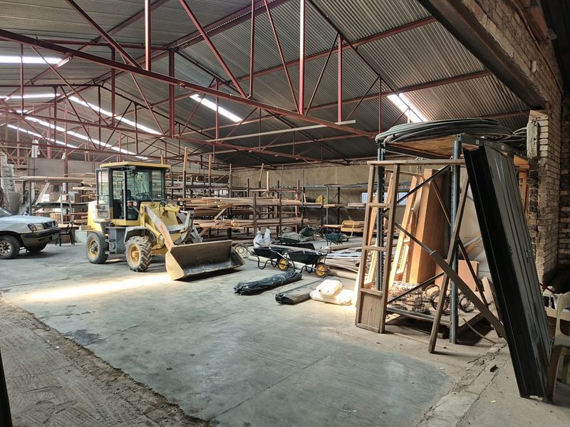 Spacious industrial warehouse area featuring exposed steel roof trusses, concrete flooring, and extensive built-in shelving for storage and operational use.