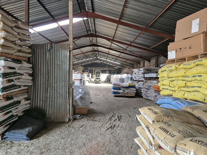 Large industrial warehouse or storage facility featuring exposed steel roof trusses, corrugated metal wall cladding, and a dirt floor.