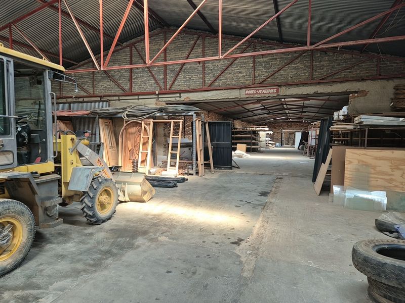 Spacious industrial warehouse featuring exposed steel roof trusses, brick walls, and concrete flooring, currently utilized for storage and industrial operations.