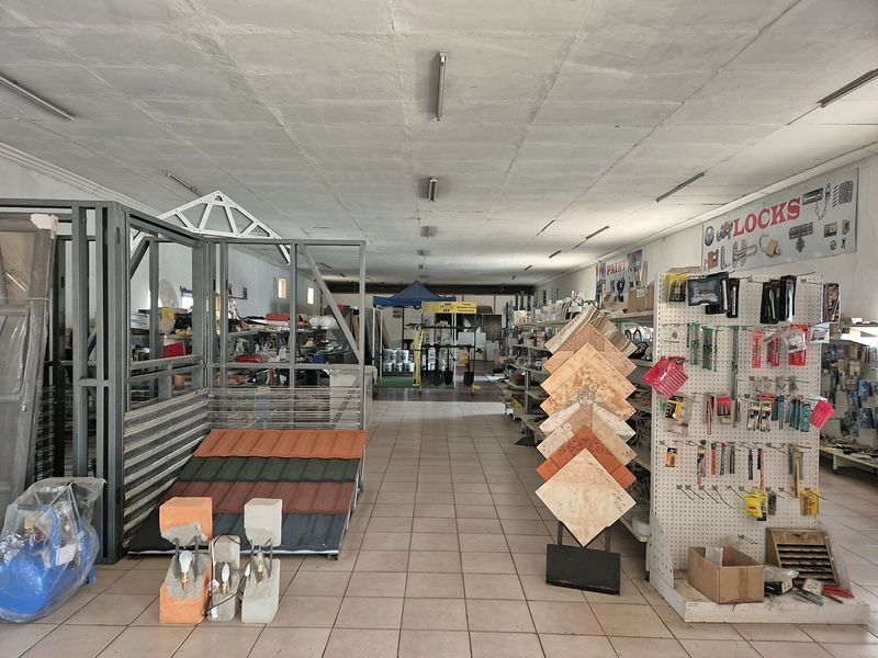 Spacious industrial retail showroom featuring tiled flooring and overhead fluorescent lighting, currently utilized for hardware and building material display.