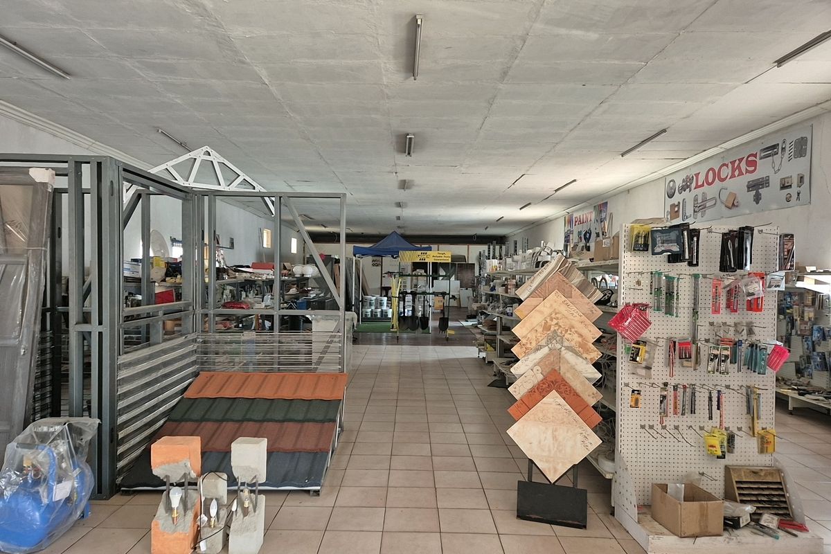 Spacious industrial retail showroom featuring tiled flooring and overhead fluorescent lighting, currently utilized for hardware and building material display.