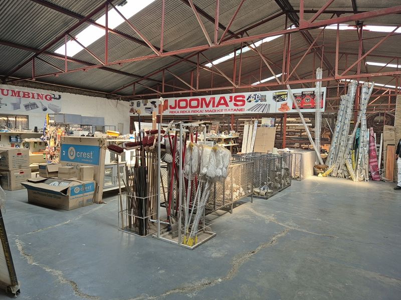 Spacious industrial warehouse interior featuring exposed steel roof trusses, corrugated metal roofing, and durable concrete flooring with wire mesh storage partitions.