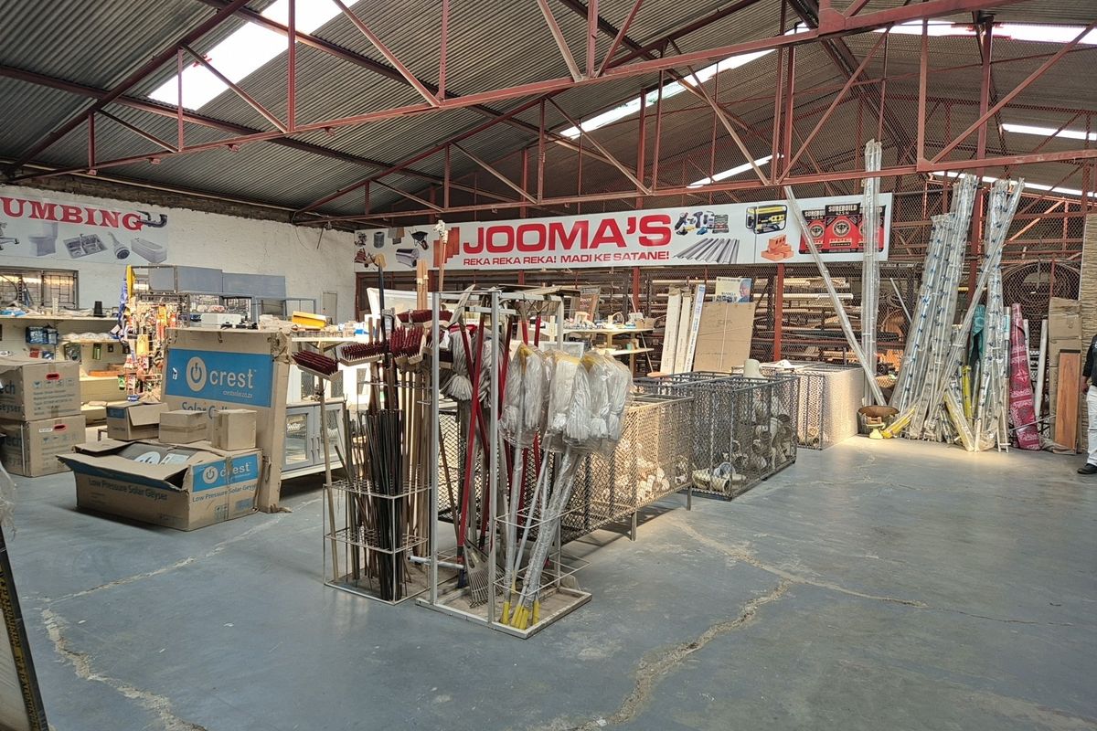 Spacious industrial warehouse interior featuring exposed steel roof trusses, corrugated metal roofing, and durable concrete flooring with wire mesh storage partitions.