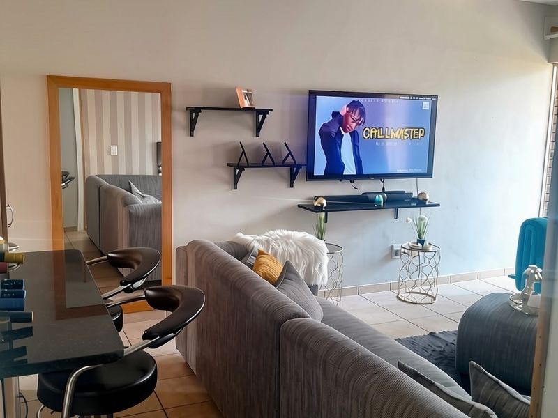 A living room area featuring tiled flooring, a drop ceiling, and wall-mounted shelving units, providing a functional and open living space.