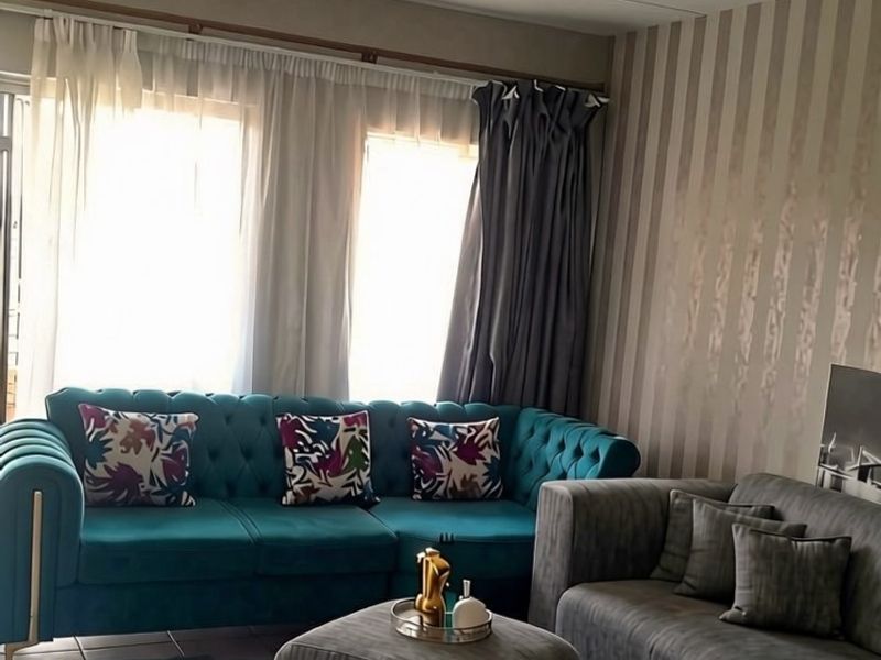 A comfortable living room featuring tiled flooring and large windows with curtain tracks, providing ample natural light.