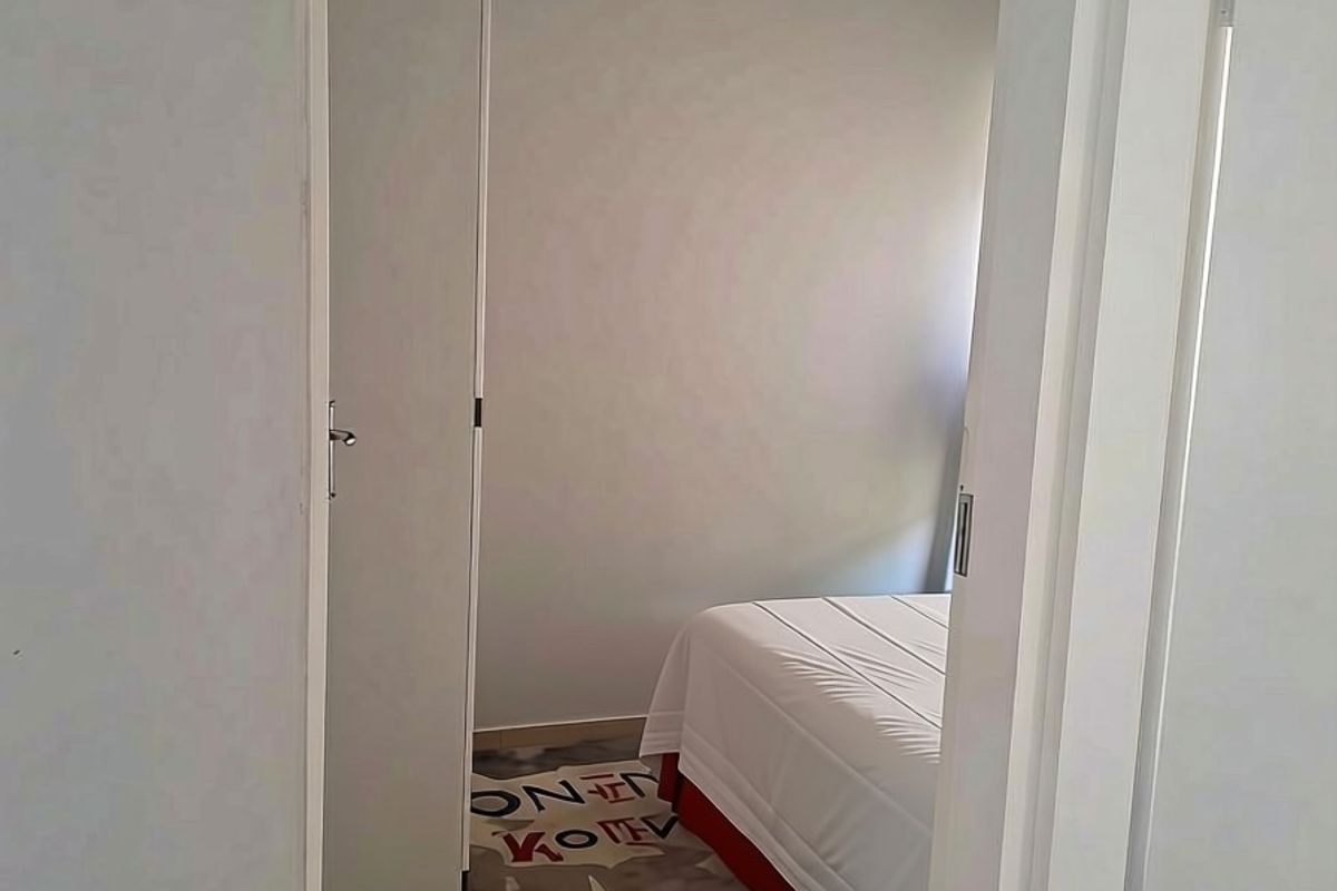 A view into a bedroom featuring tiled flooring and a built-in cupboard, viewed through a doorway.