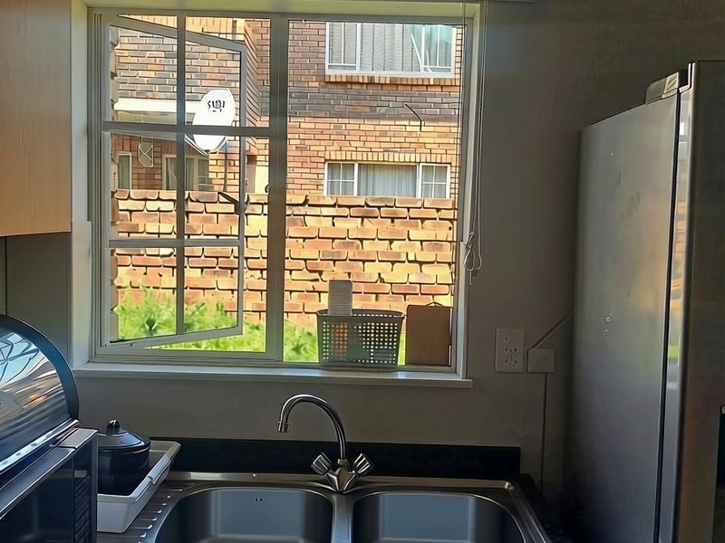 A functional kitchen area featuring a double bowl stainless steel sink, granite countertops, and wooden cabinetry with a view of the exterior.
