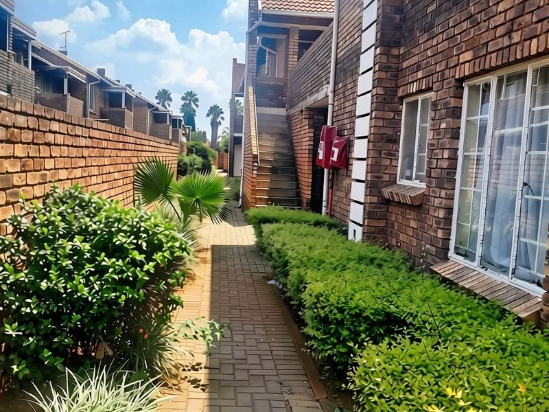 A view of the apartment complex exterior featuring a paved walkway, face brick walls, and an external staircase leading to upper levels.