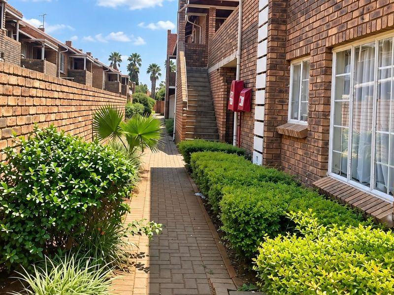 A well-maintained exterior walkway featuring brick facade construction, paved pathways, and established garden landscaping between apartment units.