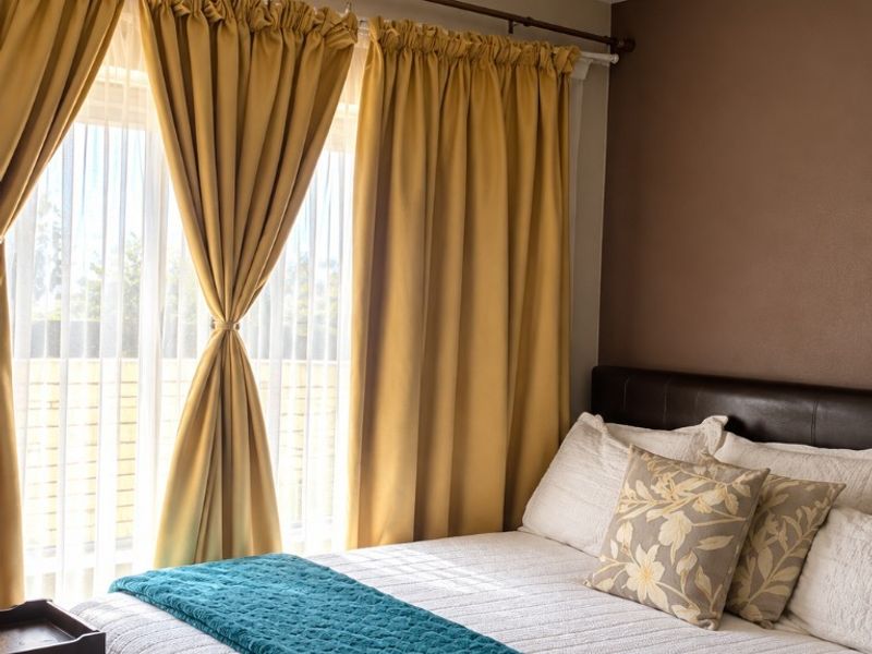 A cozy bedroom featuring a large window with curtains and a central ceiling light fixture.