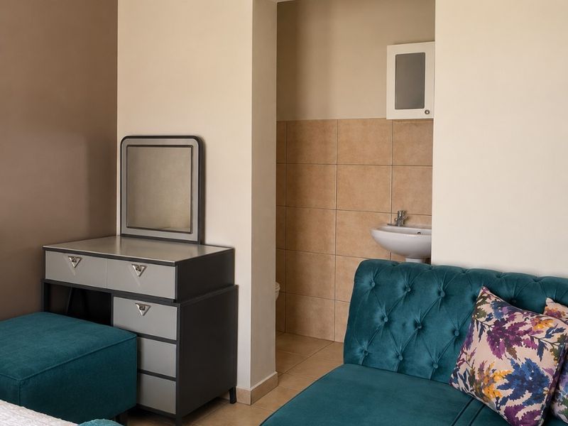 A bedroom featuring tiled flooring and an open-plan en-suite area with a wall-mounted basin and storage cabinet.
