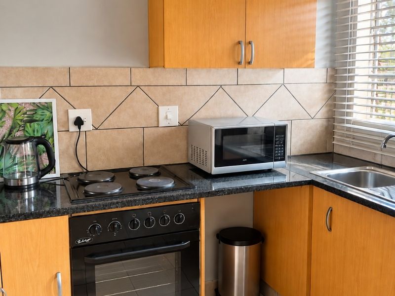 A functional kitchen featuring wood-veneer cabinetry, granite countertops, a built-in oven with electric hob, and a tiled backsplash.