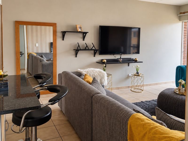 Open-plan living area featuring tiled flooring, a granite breakfast bar, and wall-mounted shelving, creating a functional and connected space.