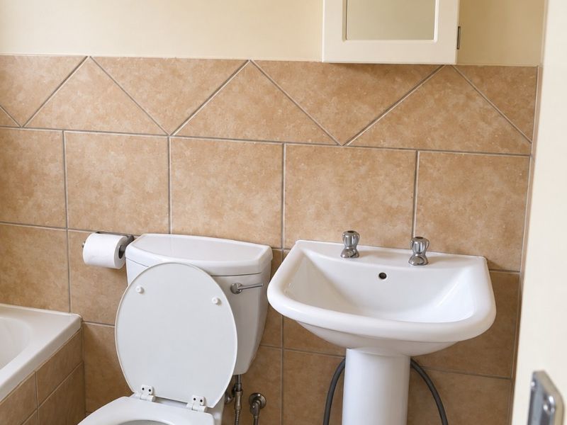 A functional bathroom featuring a pedestal basin, toilet, and wall-mounted medicine cabinet with neutral tiled walls and flooring.