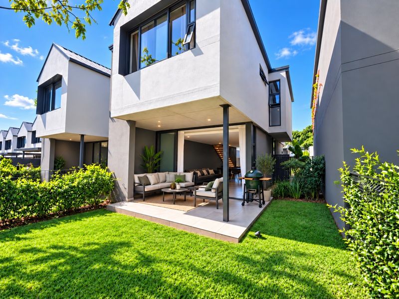 A modern townhouse rear elevation featuring a covered tiled patio, seamless indoor-outdoor flow through sliding doors, and a well-maintained private garden.