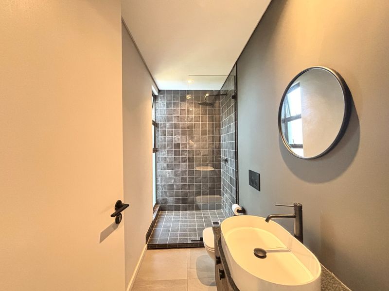 Modern bathroom featuring a walk-in shower with dark tiled walls, a contemporary vessel sink, and sleek matte black fixtures.