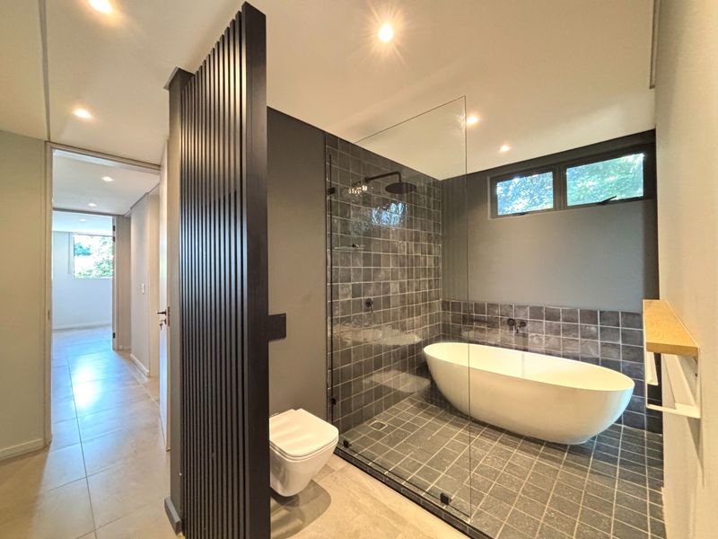 Modern, high-end bathroom featuring a freestanding bathtub, walk-in shower with glass partition, wall-mounted toilet, and a stylish slatted timber privacy screen.