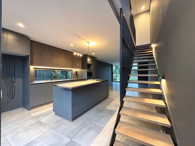 Modern open-plan kitchen featuring a central island, sleek cabinetry, and a contemporary staircase with timber treads and metal balustrades.